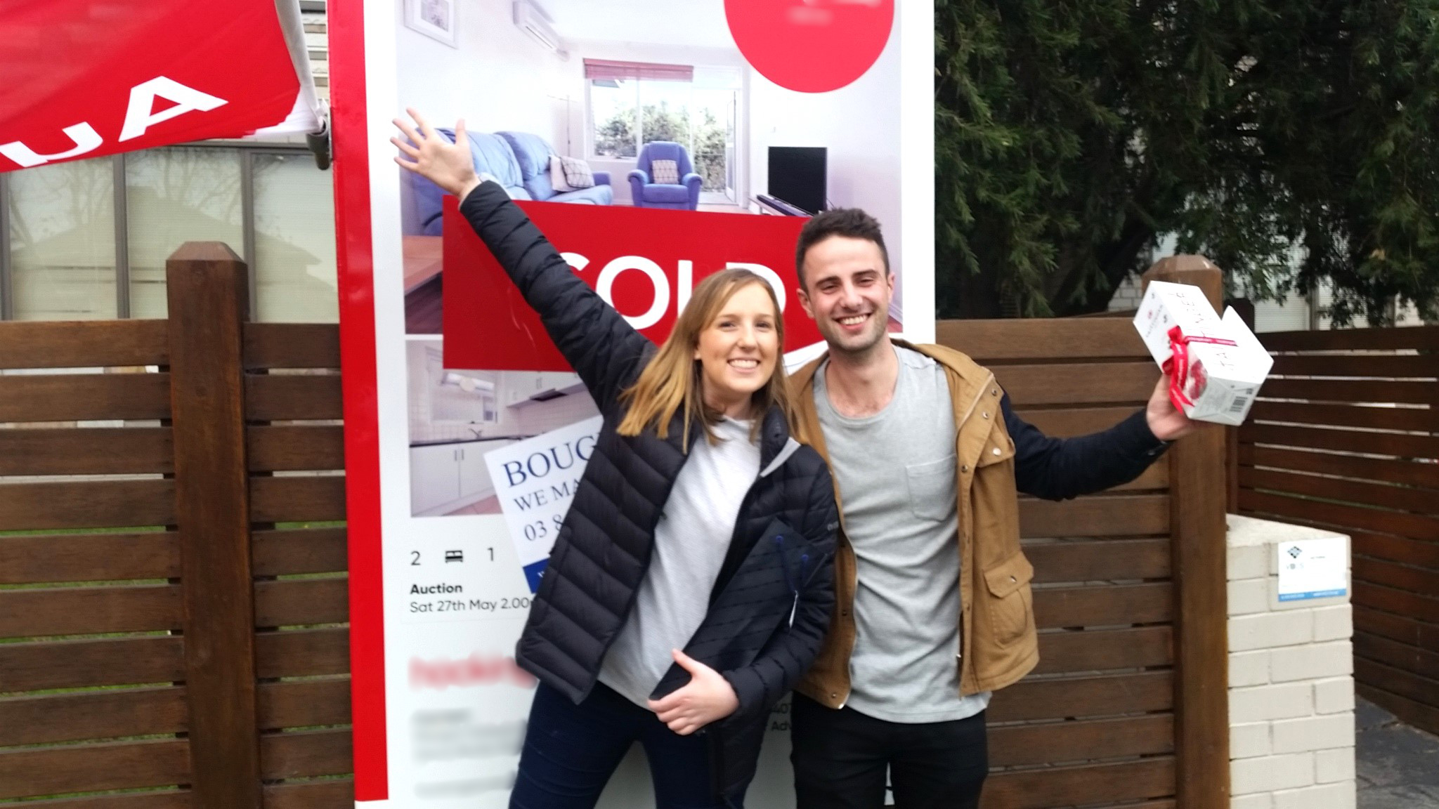 A couple standing next to a SOLD sign outside their newly purchased property with the help of Wendy Chamberlain of Chamberlain Property Advocates.