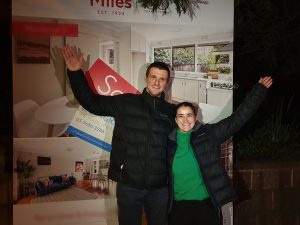 A couple infront of the property board of their recently purchased home with help of Wendy Chamberlain.